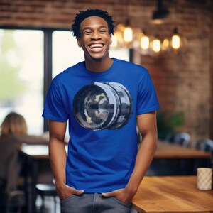 May include: A royal blue t-shirt with a watercolor-style image of a camera lens.