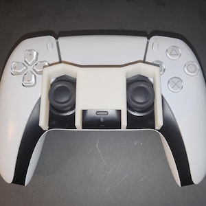 May include: A white PlayStation 5 DualSense controller with a 3D printed white attachment that adds two extra buttons to the controller.