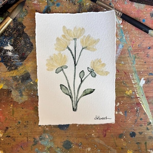 May include: A watercolor painting on textured paper featuring a cluster of four pale yellow flowers with dark green stems and leaves. The artwork is signed in the bottom right corner with the handwritten text Hbach in black ink.