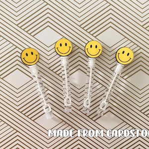 May include: Four clear plastic bubble wands with yellow smiley face toppers. The smiley faces are made from cardstock. The background is a white and gold geometric pattern. The text "MADE FROM CARDSTOCK" is at the bottom.