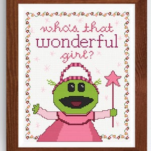 May include: Cross stitch pattern featuring a green character with a pink dress and a star wand. The text "Who's that wonderful girl?" is above the character.