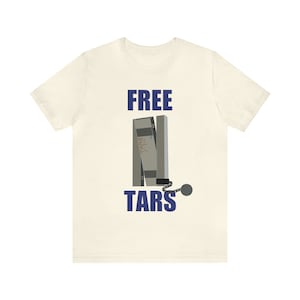 May include: A white t-shirt with the text "FREE TARS" in blue lettering. The text is above a graphic of a stack of cassette tapes with a chain and ball attached.