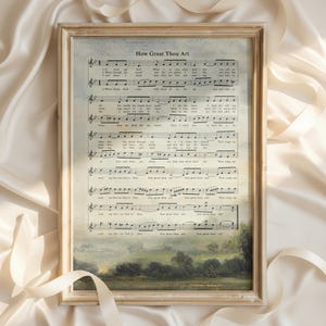 Puede incluir: Un marco de madera rectangular que contiene una impresión del himno How Great Thou Art, con notación musical y letra superpuesta sobre una pintura de paisaje de un campo verde y árboles bajo un cielo suave y nublado en tonos tierra.