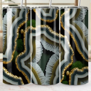 Peut inclure: Trois gobelets en acier inoxydable avec un motif agate. Le motif présente des couches de noir, de blanc, d'or et de vert, créant un motif de type géode. Chaque gobelet est doté d'une paille argentée.
