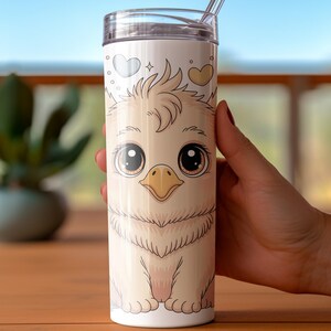 May include: A white tumbler featuring a cartoon bird design with large eyes and a yellow beak. The tumbler has a clear lid and a straw. The bird design includes hearts and stars. The tumbler is held by a person.