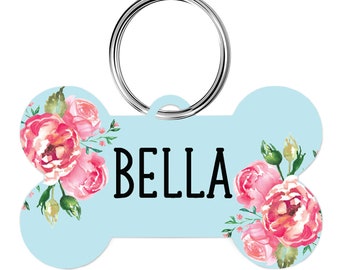 May include: A light blue bone-shaped dog tag with a floral design and the name "BELLA" printed in black.