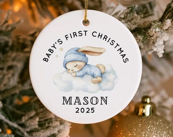 May include: White ceramic Christmas ornament with gold string. The ornament features a sleeping baby bunny in a blue onesie and hat on a cloud, with the text "BABY'S FIRST CHRISTMAS" and the name "MASON" and the year "2025".