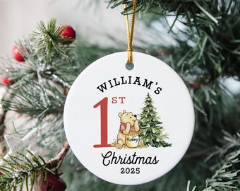 May include: A white ceramic Christmas ornament with the text "William's 1st Christmas 2025". The ornament features a cartoon illustration of Winnie the Pooh with a honey pot and a Christmas tree. A gold string is attached for hanging.