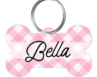 May include: Pink and white gingham dog bone shaped tag with a silver ring and the name "Bella" written in black cursive.