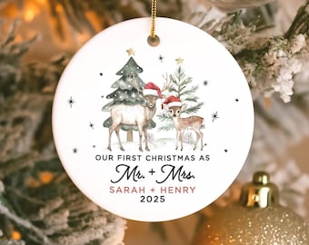 May include: Round white ceramic Christmas ornament with a gold hanging string. The ornament features a watercolour illustration of two deer wearing Santa hats, Christmas trees, and the text "OUR FIRST CHRISTMAS AS Mr. + Mrs. SARAH + HENRY 2025."