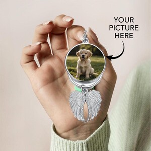 May include: A silver-colored memorial ornament with a photo of a golden retriever puppy. The ornament has a pair of detailed angel wings below the photo. The text "YOUR PICTURE HERE" is visible.