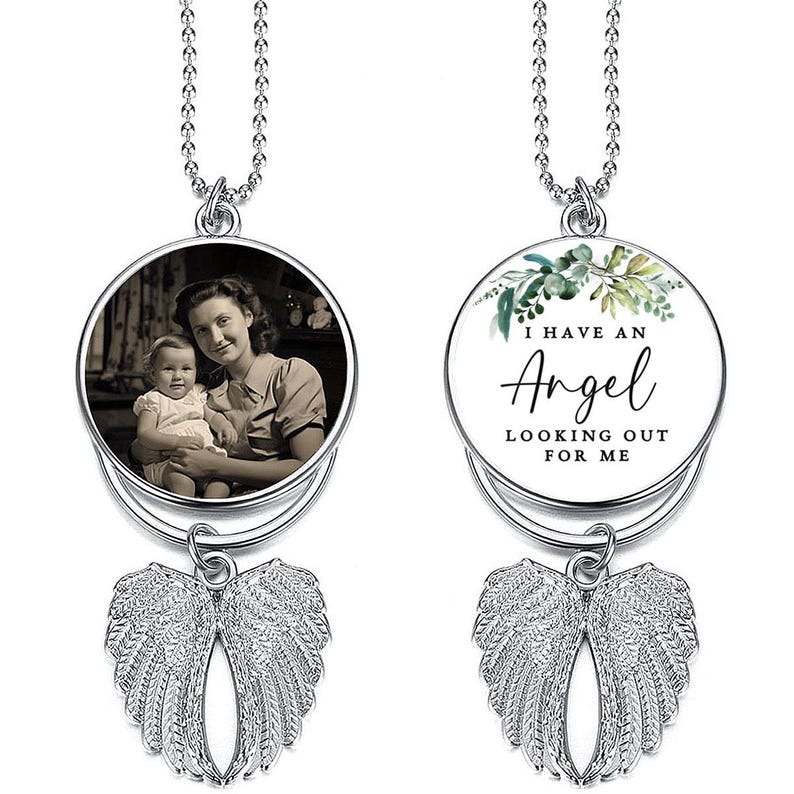May include: Two silver-toned memorial necklaces. One features a black and white photo of a woman and child. The other has the text "I HAVE AN Angel LOOKING OUT FOR ME" with a floral design. Both have wing charms.