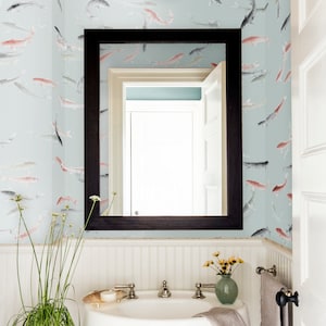 Könnte beinhalten: Ein weißes Waschbecken mit einem verchromten Wasserhahn in einem Badezimmer mit weißen Wandverkleidungen und blauer Tapete mit Fischmuster. Eine Topfpflanze steht auf einem Holzhocker neben dem Waschbecken.
