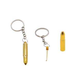 May include: Two gold-colored bullet-shaped keychains with metal rings and chains. One keychain is closed, while the other is open, revealing a thin, gold-colored metal tool attached to the cap. A separate gold bullet-shaped casing is also shown.