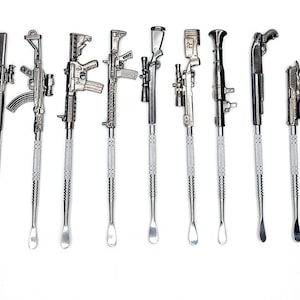 Puede incluir: Una colección de nueve herramientas dab de metal plateado, cada una diseñada con una forma de arma de fuego diferente. Las herramientas tienen un mango texturizado y un extremo pequeño en forma de cuchara. Las armas de fuego incluyen rifles, escopetas y pistolas.