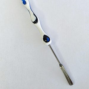 May include: A white and blue decorative tool with a stainless steel blade. The handle has a curved design with blue and black accents. The tool is designed for a specific purpose, likely in the kitchen or for crafts.