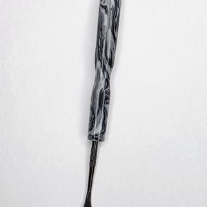 May include: A diamond painting drill pen featuring a thick, contoured handle with a marbled black, gray, and white pattern. The tool includes a slim, matte black metal tip with a small, rounded, spoon-like end for picking up small craft items.