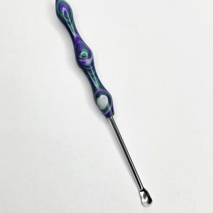 May include: A purple, green, and white marbled resin tool with a stainless steel scoop end. The tool has a curved, ergonomic handle and is designed for scooping. The handle is approximately 10 cm long.