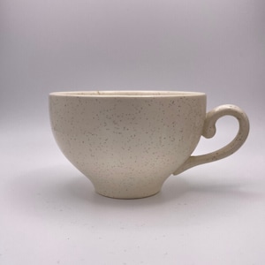 May include: A white ceramic teacup with a speckled finish and a curved handle.