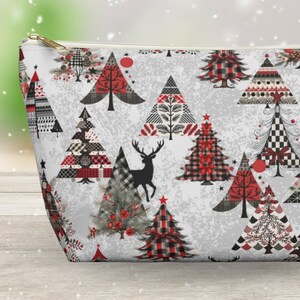 Può includere: Un beauty case con cerniera con un motivo festivo di alberi di Natale in rosso, nero e bianco. Gli alberi presentano vari disegni, tra cui quadri e motivi geometrici, su uno sfondo grigio chiaro. Una cerniera dorata e una silhouette di cervo completano il design.