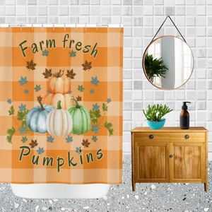 K&ouml;nnte beinhalten: Orange karierter Duschvorhang mit dem Text "Farm fresh pumpkins" und Illustrationen von K&uuml;rbissen und Bl&auml;ttern. Der Duschvorhang befindet sich in einem Badezimmer mit einem Holzschrank, Spiegel und Zubeh&ouml;r.