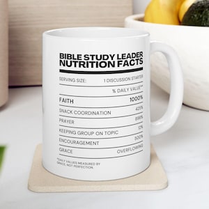 May include: White ceramic mug with the text "BIBLE STUDY LEADER NUTRITION FACTS". The mug features a nutrition facts label with values for Faith, Snack Coordination, Prayer, and more. The mug sits on a beige coaster.