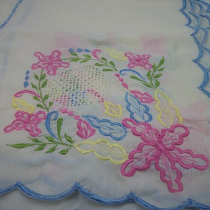May include: White embroidered tablecloth with a scalloped edge and a floral design in pink, blue, yellow, and green.