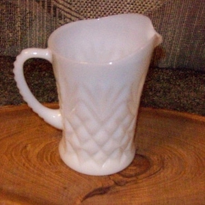 May include: White milk glass pitcher with a diamond pattern. The pitcher has a handle and a spout.