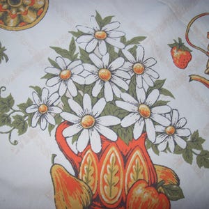 May include: A white tablecloth with a floral design featuring daisies, strawberries, and pears. The daisies are in a red vase. A teapot and a decorative plate are also visible.