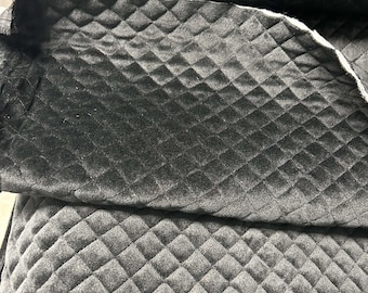 Op de afbeelding: Close-up van zwarte gewatteerde stof met een ruitpatroon. De stof heeft een zachte, fluweelzachte textuur en een subtiele glans. Het quilten creëert een verhoogd, dimensionaal effect. De stof wordt waarschijnlijk gebruikt voor bekleding of kleding.