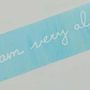 May include: A rectangular light blue sticker with the handwritten words "I am very alive" in white cursive script. The sticker has a watercolor-like effect.