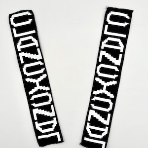 May include: Two black fabric patches with white pixelated text that reads "KIDZORD". The patches are rectangular with a frayed edge. The background is plain white.