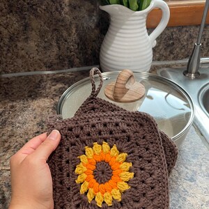 May include: Two brown crocheted pot holders with a sunflower design in the center. The sunflower is made with yellow and orange yarn.