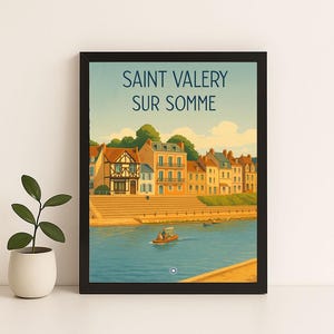 Op de afbeelding: Een ingelijste kunstdruk met een vintage reisaffiche voor Saint Valery sur Somme. Het kunstwerk toont kleurrijke gebouwen langs een rivier, een boot en de tekst "SAINT VALERY SUR SOMME" tegen een blauwe lucht.