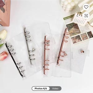 May include: Three clear plastic A5 binder covers with six-ring metal mechanisms. One binder features a silver-tone mechanism, one has a rose gold-tone mechanism, and one includes a rose gold-tone snap button closure on the front cover.