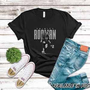 May include: Black t-shirt with a white graphic of a basketball player dribbling the ball. The graphic includes the text "Trinity Rodman #2".