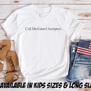 May include: White t-shirt with the text "Call Me Ceee-Champion." on a wooden background. The shirt is available in kids sizes and long sleeve.