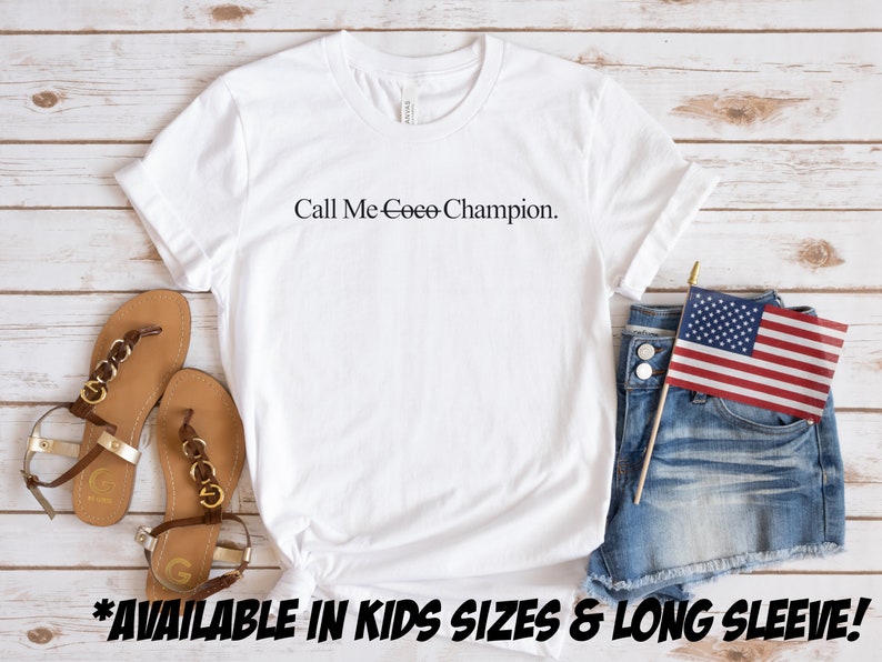May include: White t-shirt with the text "Call Me Ceee-Champion." on a wooden background. The shirt is available in kids sizes and long sleeve.