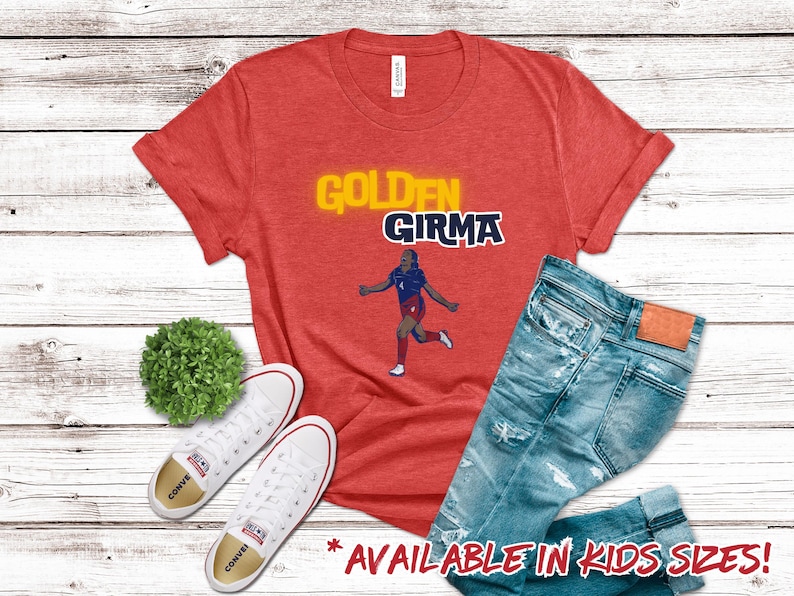 May include: Red t-shirt with a yellow and blue graphic of a soccer player with the text "Golden Girma".