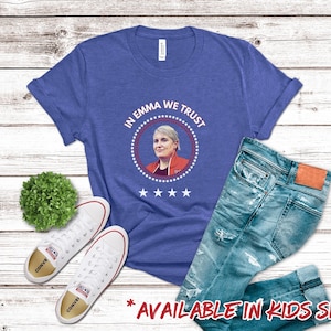 Pu&ograve; includere: Una maglietta blu reale con il testo "In Emma We Trust" in un design a sigillo presidenziale rosso, bianco e blu. Il sigillo presenta una foto di una donna con i capelli corti e biondi. La maglietta &egrave; disponibile in taglie per bambini.