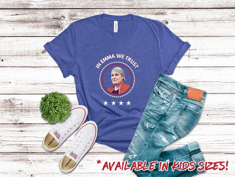 Pu&ograve; includere: Una maglietta blu reale con il testo "In Emma We Trust" in un design a sigillo presidenziale rosso, bianco e blu. Il sigillo presenta una foto di una donna con i capelli corti e biondi. La maglietta &egrave; disponibile in taglie per bambini.