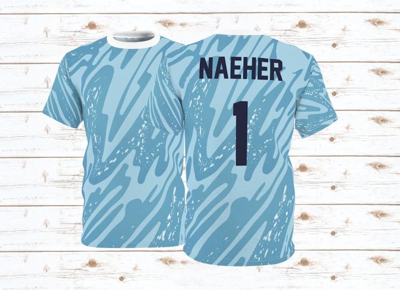 Puede incluir: Una camiseta de f&uacute;tbol azul claro con cuello blanco y un patr&oacute;n abstracto azul. La camiseta tiene el nombre "NAEHER" y el n&uacute;mero "1" impreso en la espalda.