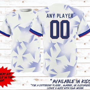 May include: White soccer jersey with blue star pattern and blue and red trim. The back displays "ANY PLAYER" above the number "00". Text on the jersey reads "AVAILABLE IN KIDS SIZES".