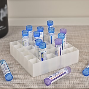May include: A white plastic organizer filled with small, cylindrical vials with blue and purple caps. Some vials are in the organizer, while others are scattered around it. A dark bottle is in the background.