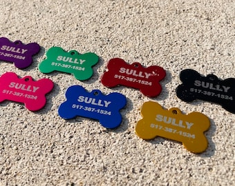 Puede incluir: Siete chapas para perros de diferentes colores, cada una con forma de hueso, con el nombre "SULLY" y el número de teléfono "517-387-1524" grabados en ellas.