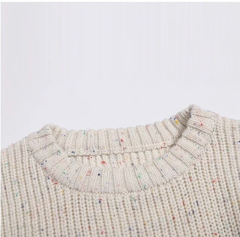 May include: Close-up of the neckline of a cream-colored sweater with a speckled pattern of multi-colored dots.