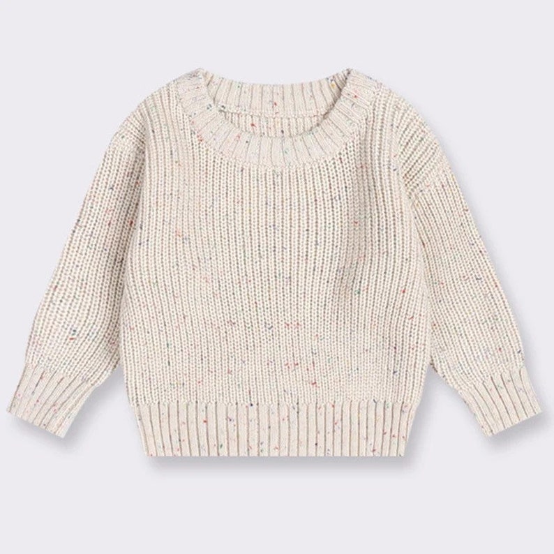 May include: A cream-colored knitted sweater with a speckled pattern. The sweater has long sleeves and a round neckline.