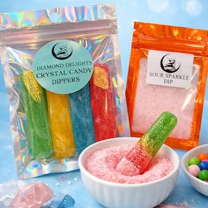 Può includere: Una selezione di candy dippers a cristallo colorati e salsa acida. I dippers sono verdi, gialli, blu e rossi, con un rivestimento glitterato. La salsa acida è rosa e in una piccola ciotola bianca. La confezione include il testo "Diamond Delights Crystal Candy Dippers" e "Sour Sparkle Dip."