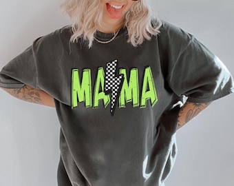 May include: A woman wearing a black trucker hat with the text "Dead Last Racing" in white, a black t-shirt with the text "Mama" in green with a lightning bolt graphic, and black leggings.