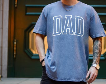 May include: A blue t-shirt with the word "DAD" printed in white on the front. The shirt is made of a soft, comfortable fabric and has a relaxed fit.